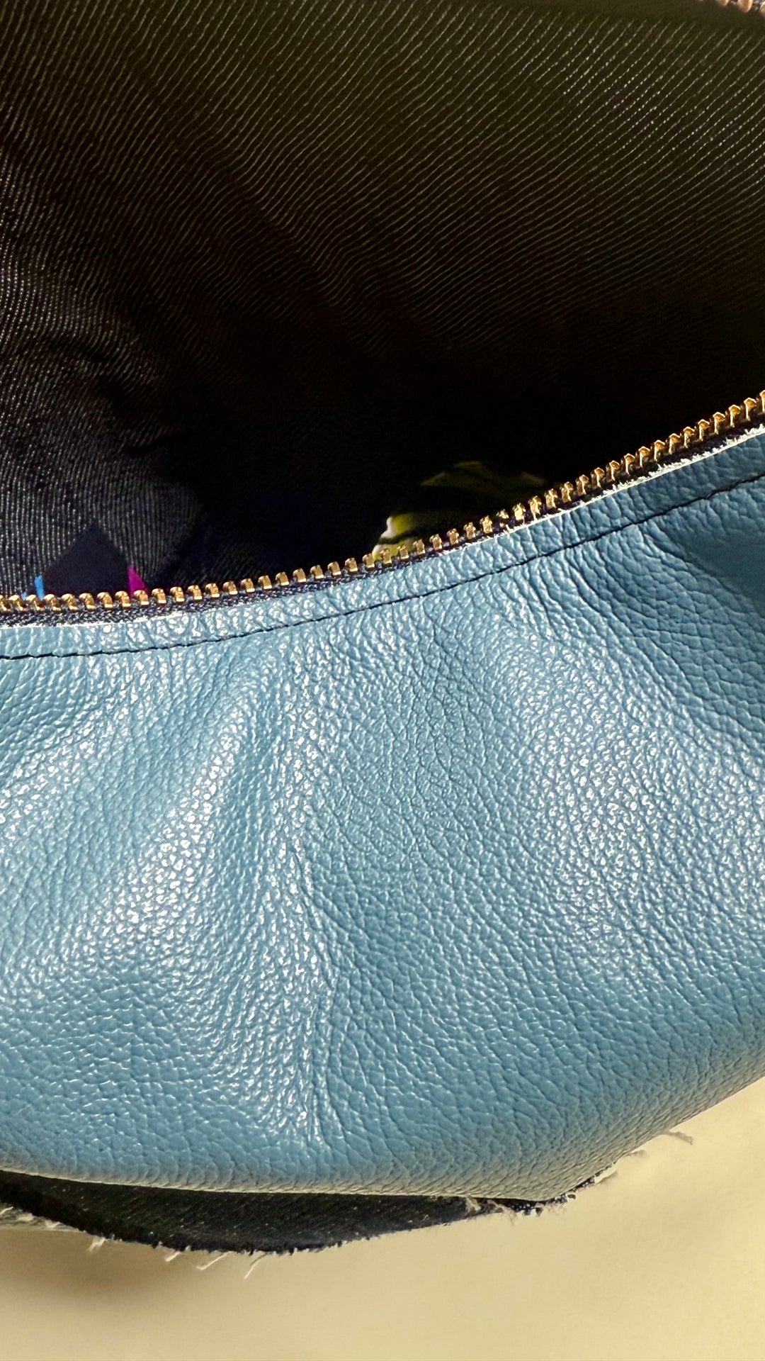 Close-up of a light blue leather bag with a gold zipper.