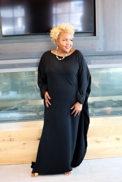 Woman in a black dress standing in front of a glass wall with a television screen above.