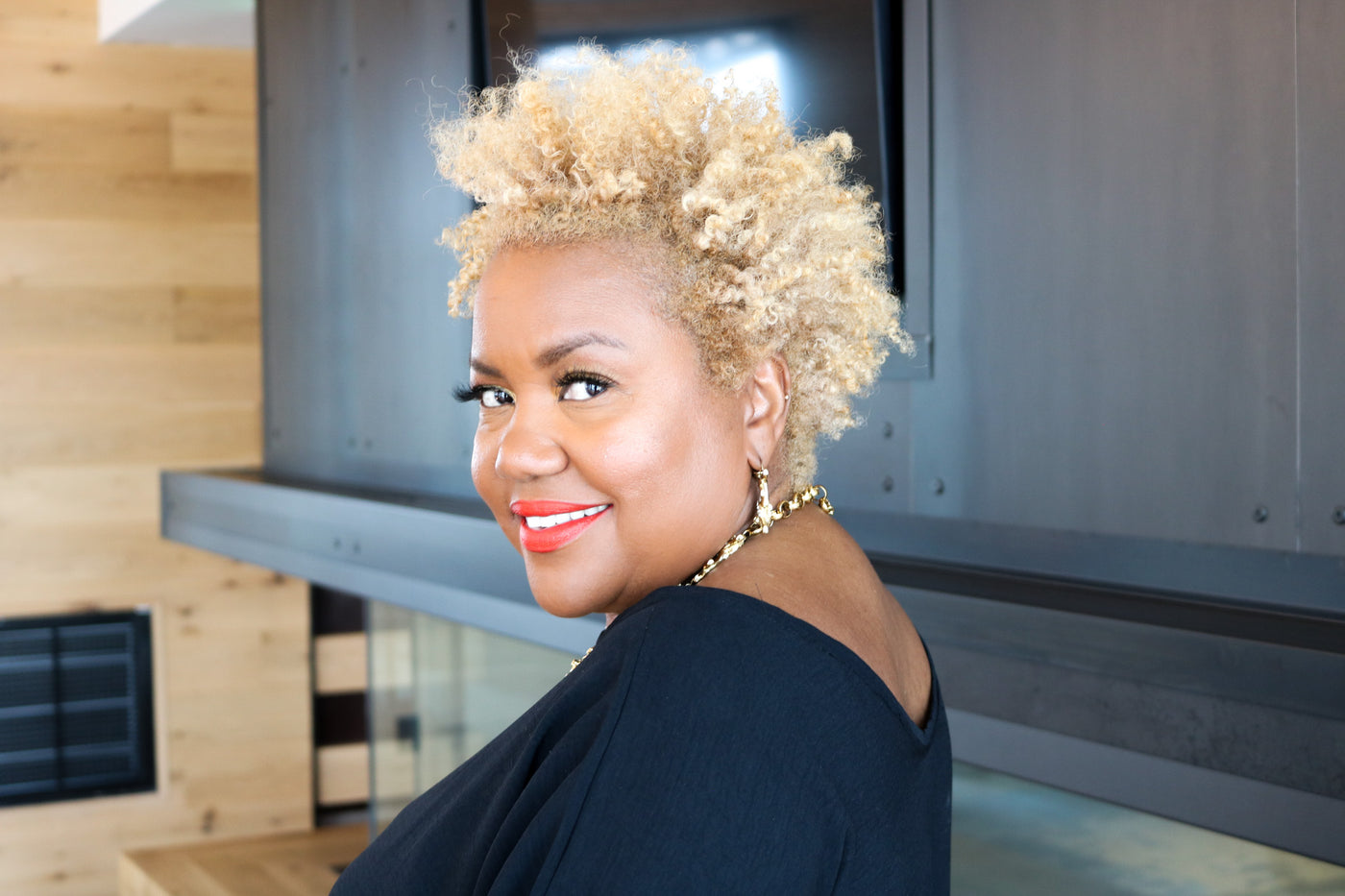 Woman with blonde hair and red lipstick smiling in a modern indoor setting
