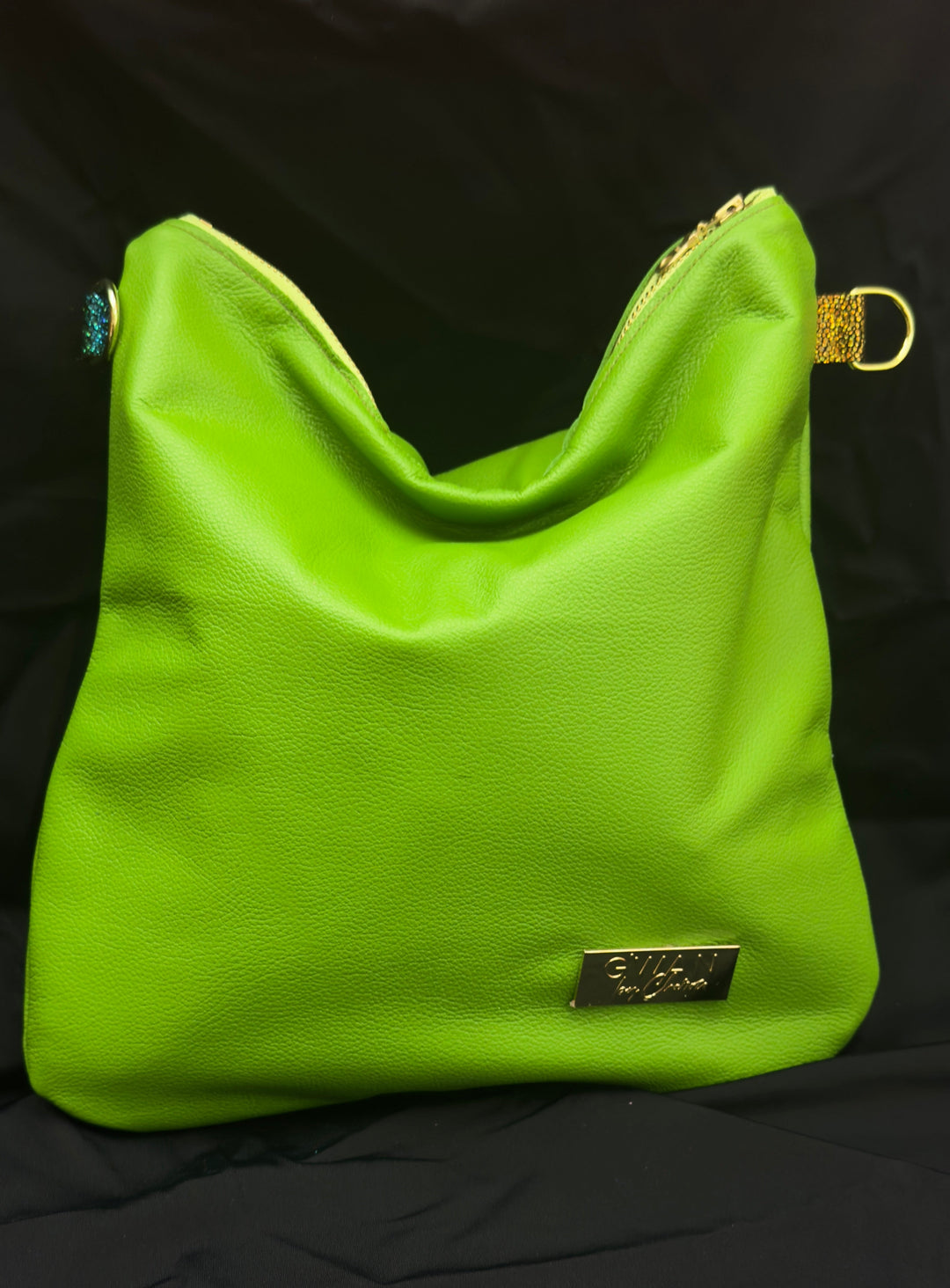 A bright lime green shoulder bag with gold-tone hardware and a small rectangular brand plaque on the front, photographed against a black fabric background.