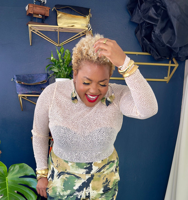 Woman in a stylish outfit with floral pants and a white top, standing in a room with a blue wall and striped floor.