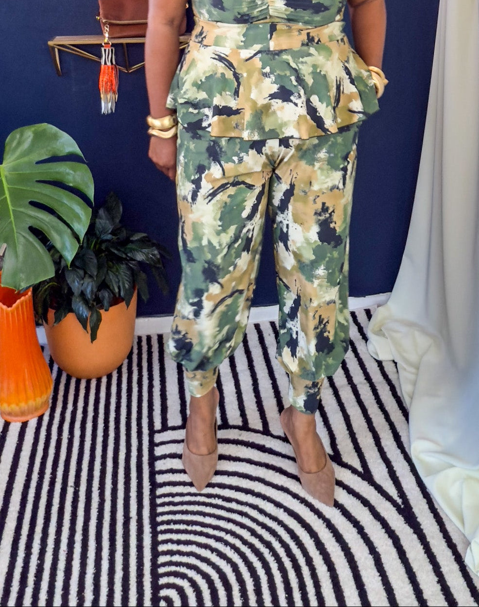 Woman in a floral outfit standing in a room with plants and shelves.