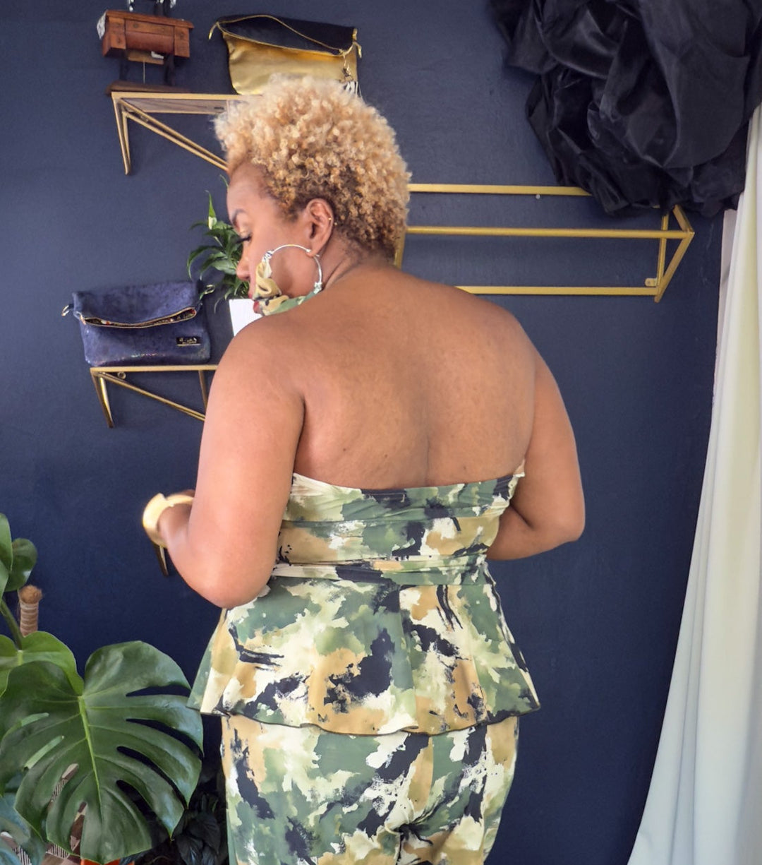 Woman in a strapless floral top and pants standing in a room with a blue wall and striped rug.