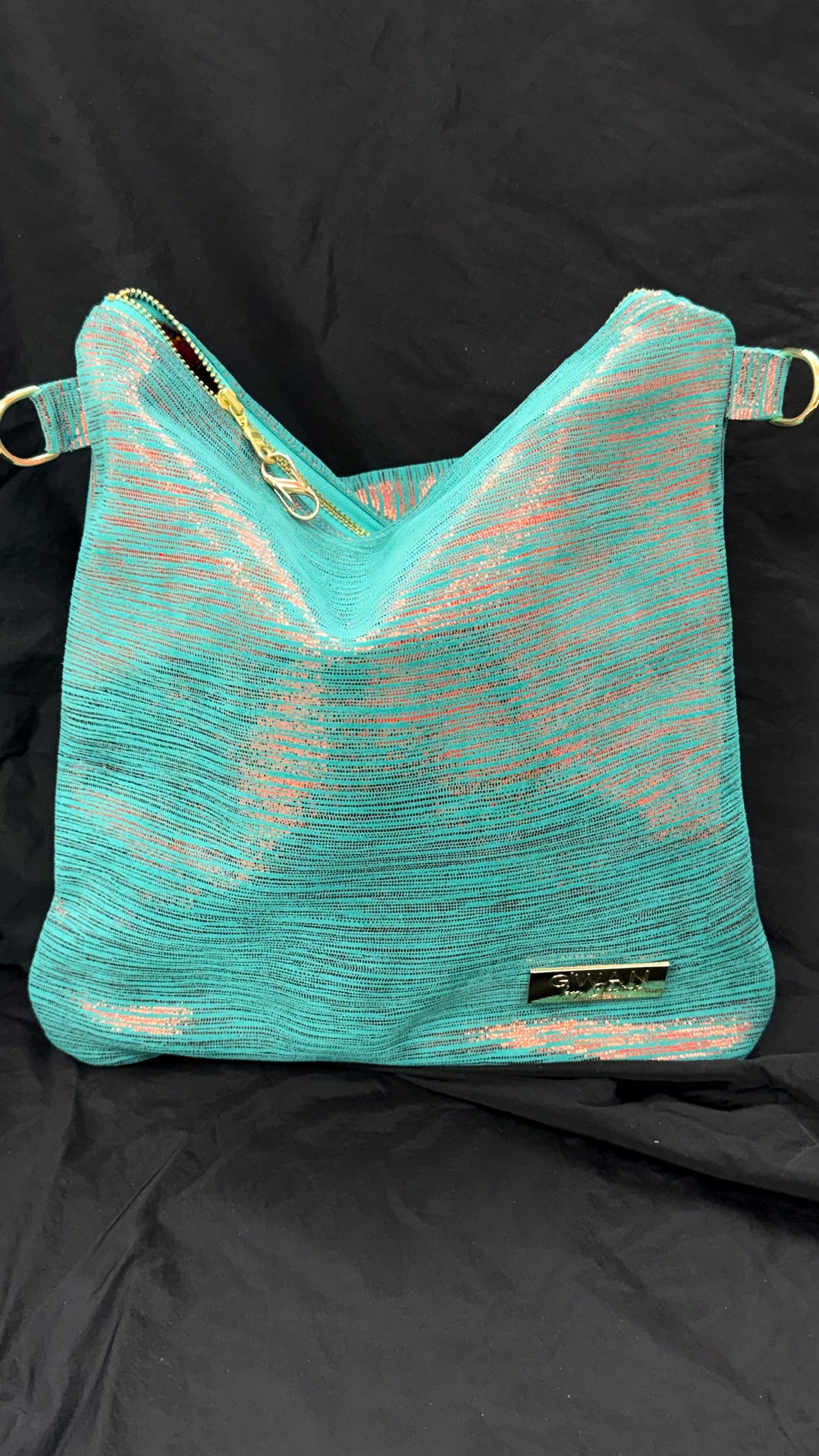 A turquoise mesh shoulder bag with gold-tone hardware and a small black brand plaque, displayed against a black fabric backdrop.