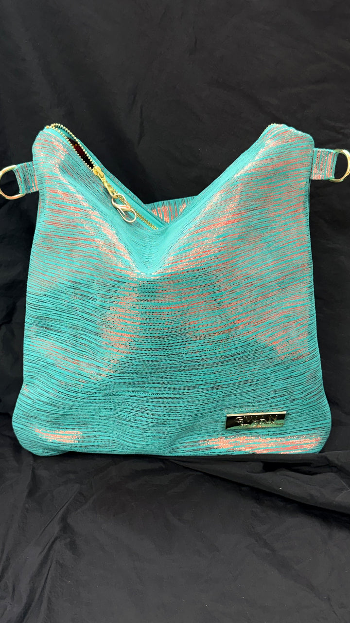 A turquoise mesh shoulder bag with gold-tone hardware and a small black brand plaque, displayed against a black fabric backdrop.