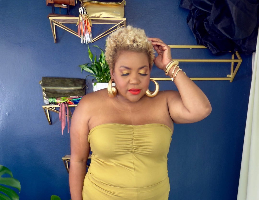 Woman in a strapless yellow jumpsuit standing against a blue wall with decorative elements.