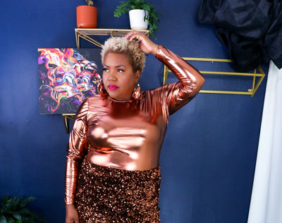 Woman in a copper metallic top and skirt standing against a blue wall with decorative elements.