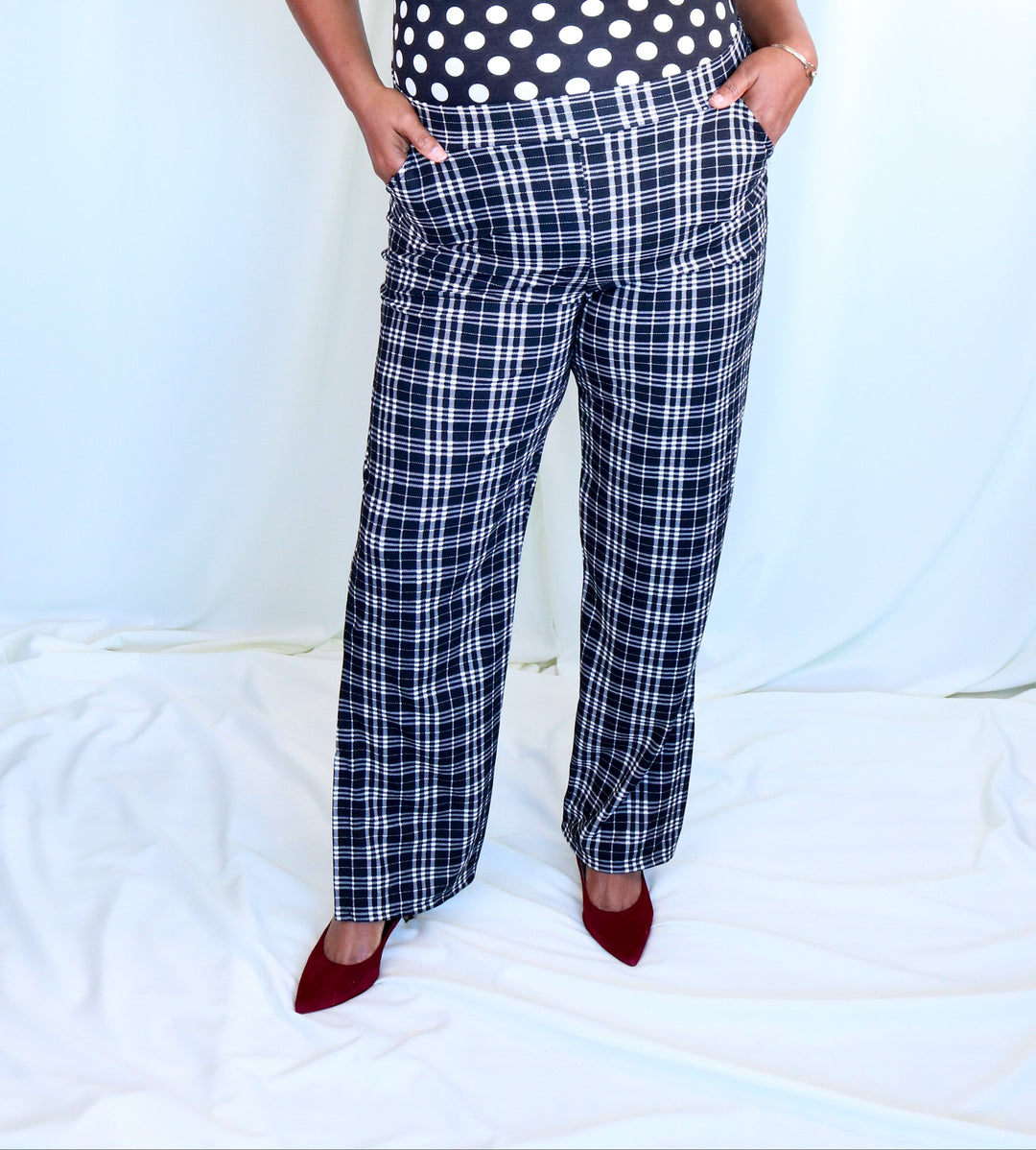 Person wearing a polka dot sleeveless top and plaid pants on a white background