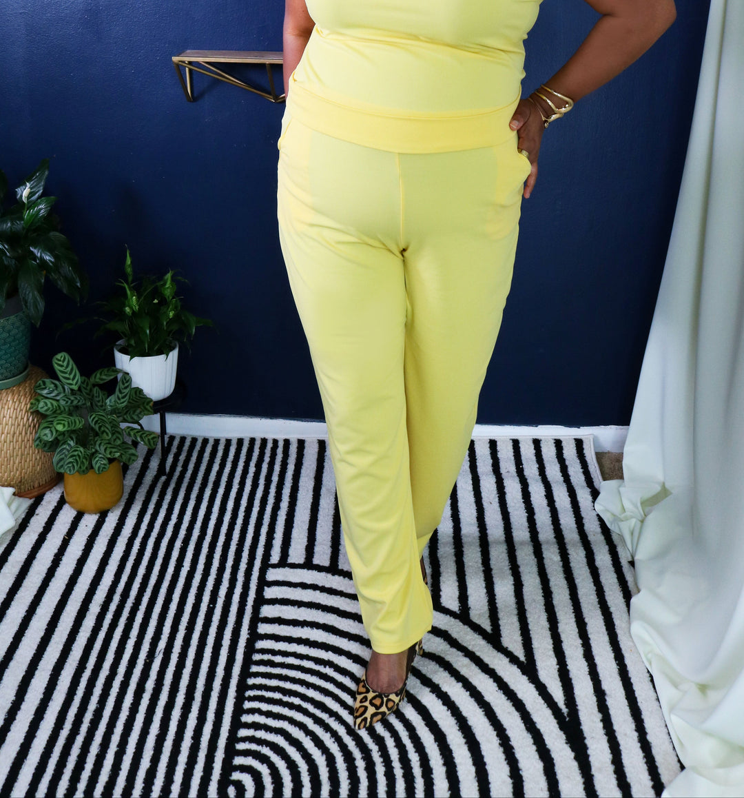 Woman in a yellow outfit standing in a room with plants and a striped rug.