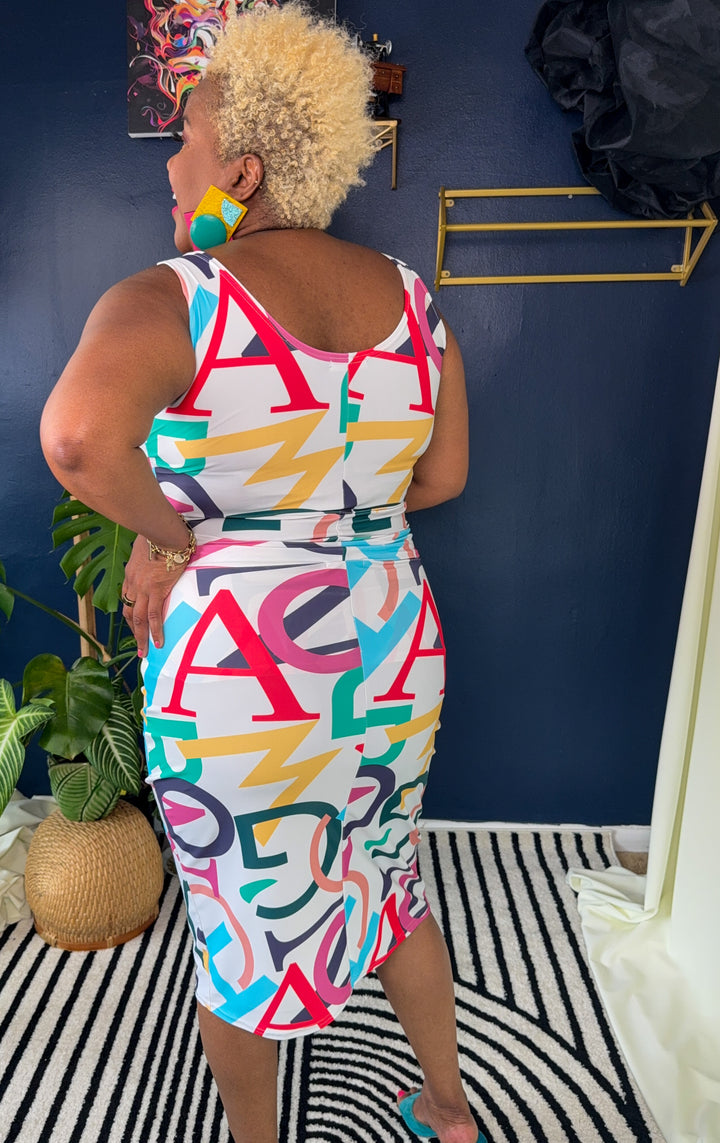 Woman wearing a colorful geometric-patterned dress standing against a blue wall.