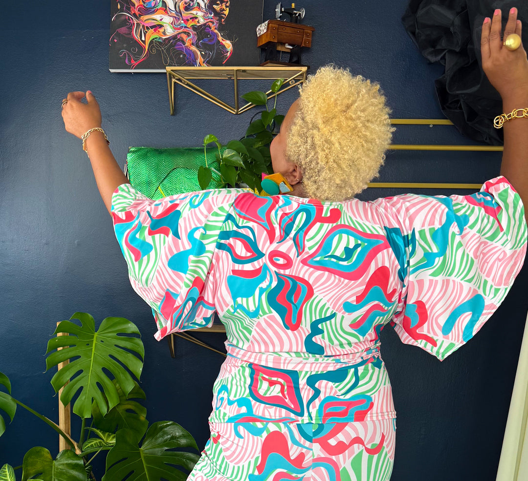Woman in a colorful dress standing in a room with a blue wall, plants, and a striped rug.