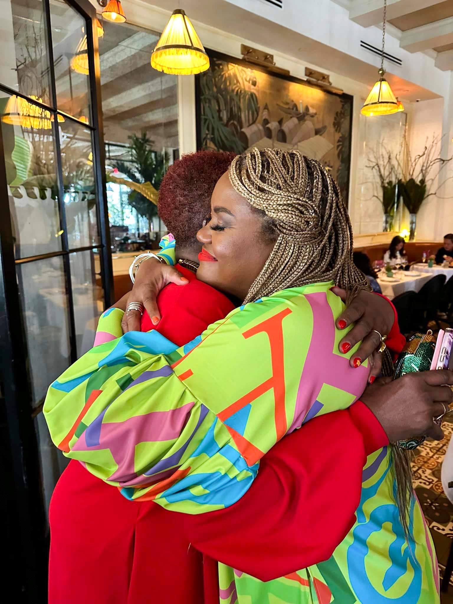 Two women hugging in a restaurant setting with colorful clothing and vibrant decor.