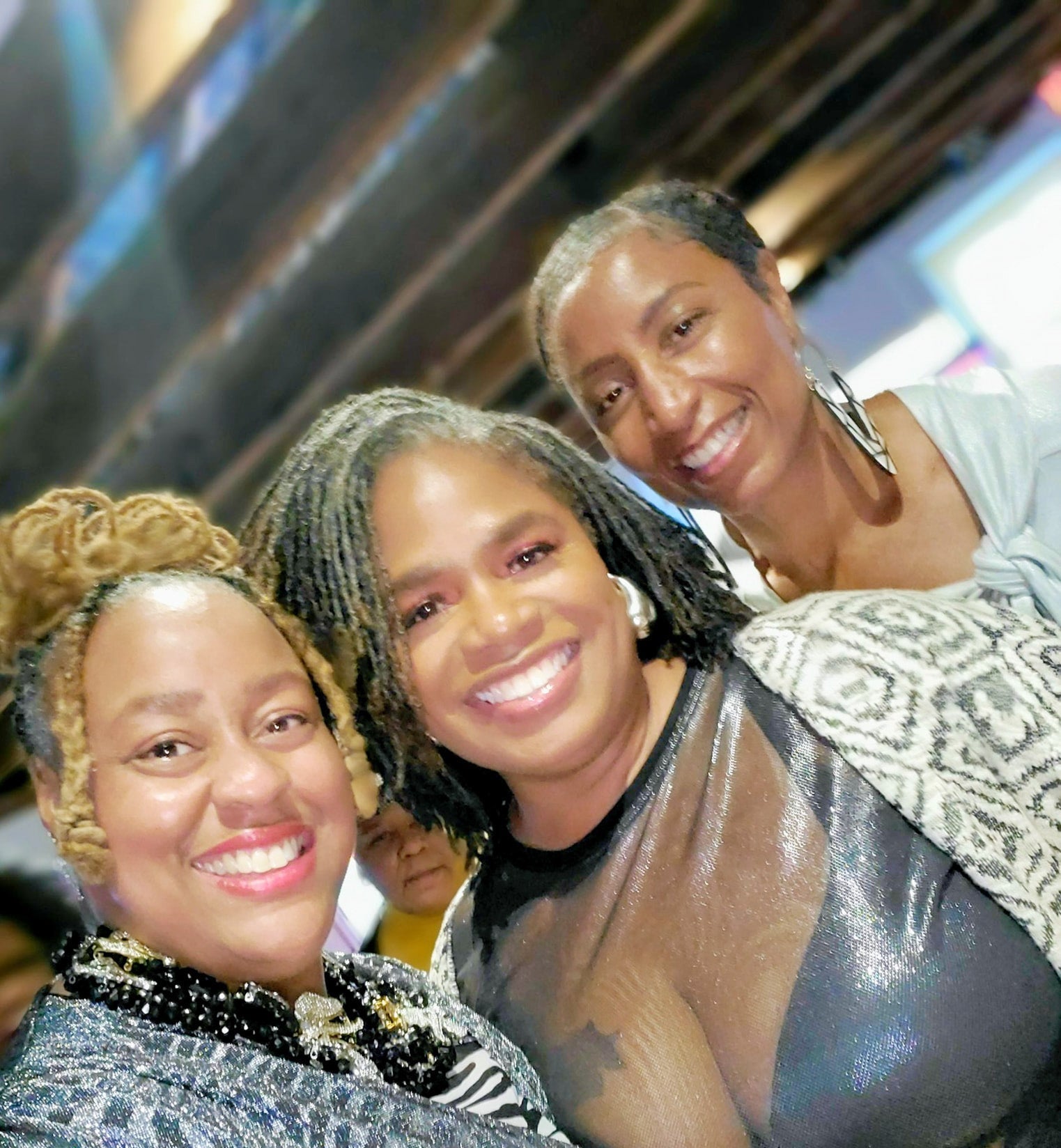 Three women posing together in a casual setting with blurred background