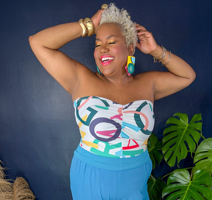 A woman modeling a strapless tube top and wide-leg pants set. The top features a colorful abstract geometric pattern with white, pink, blue, green, and orange shapes, paired with solid bright blue wide-leg pants.