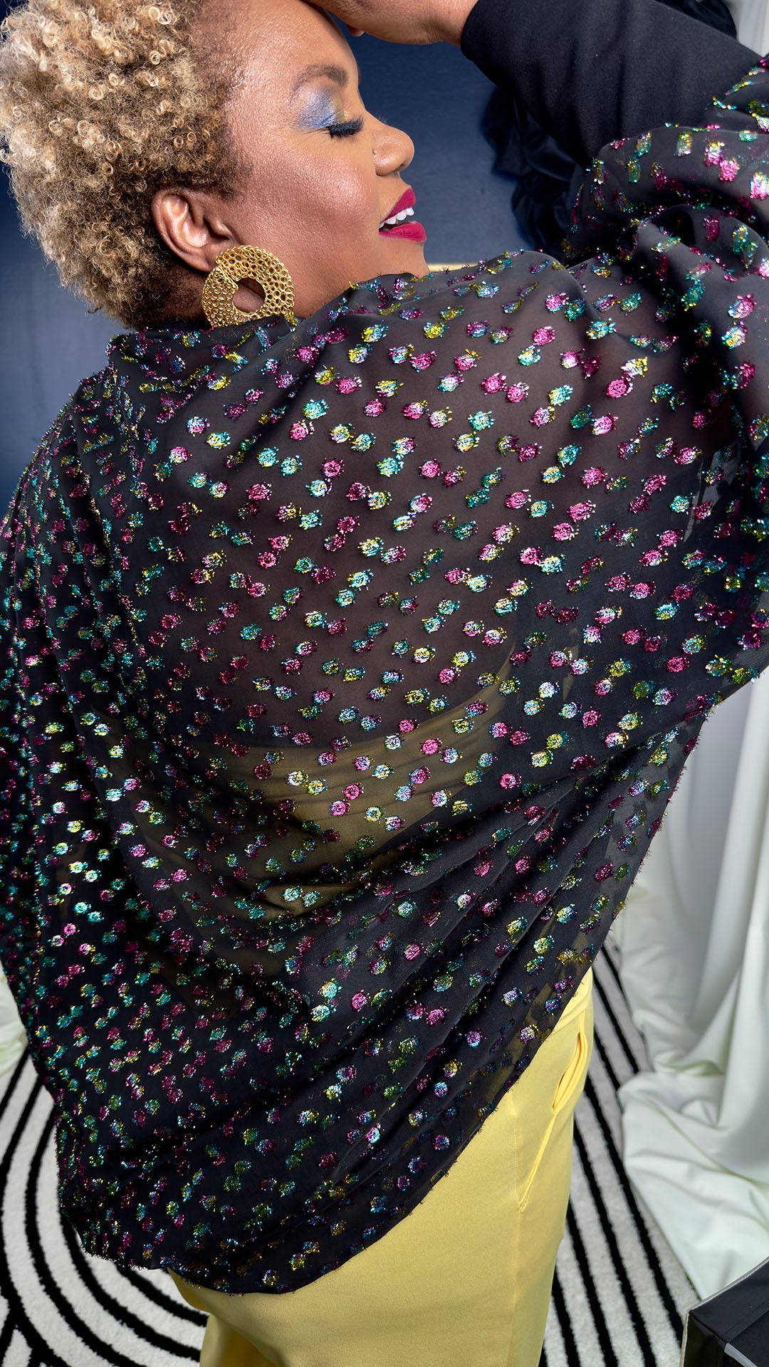 Person wearing a black floral-patterned top with colorful sequins on a black and white striped background